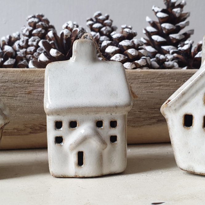 artificial wedding flowers - White ceramic house-shaped lantern with pinecones in the background