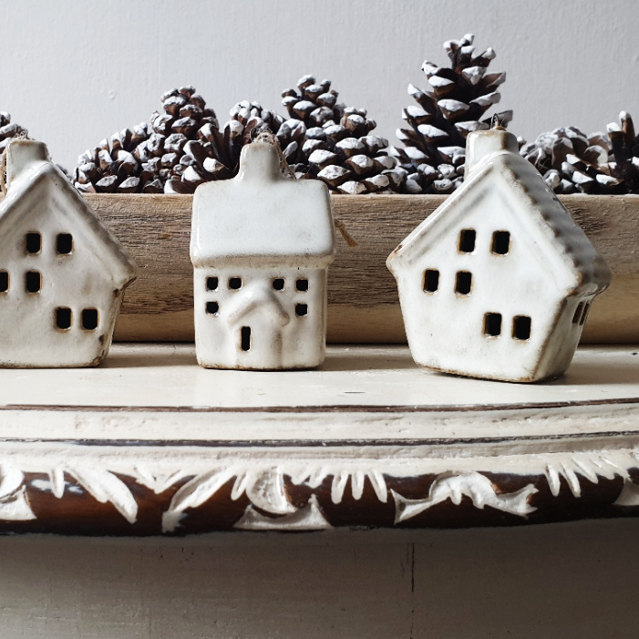 artificial wedding flowers - Three small ceramic houses with pinecones on a decorative shelf.