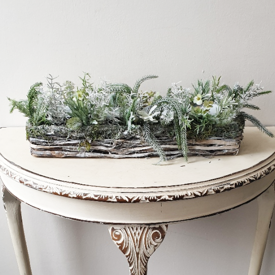 artificial wedding flowers - Decorative table with a woven basket filled with greenery on a white background