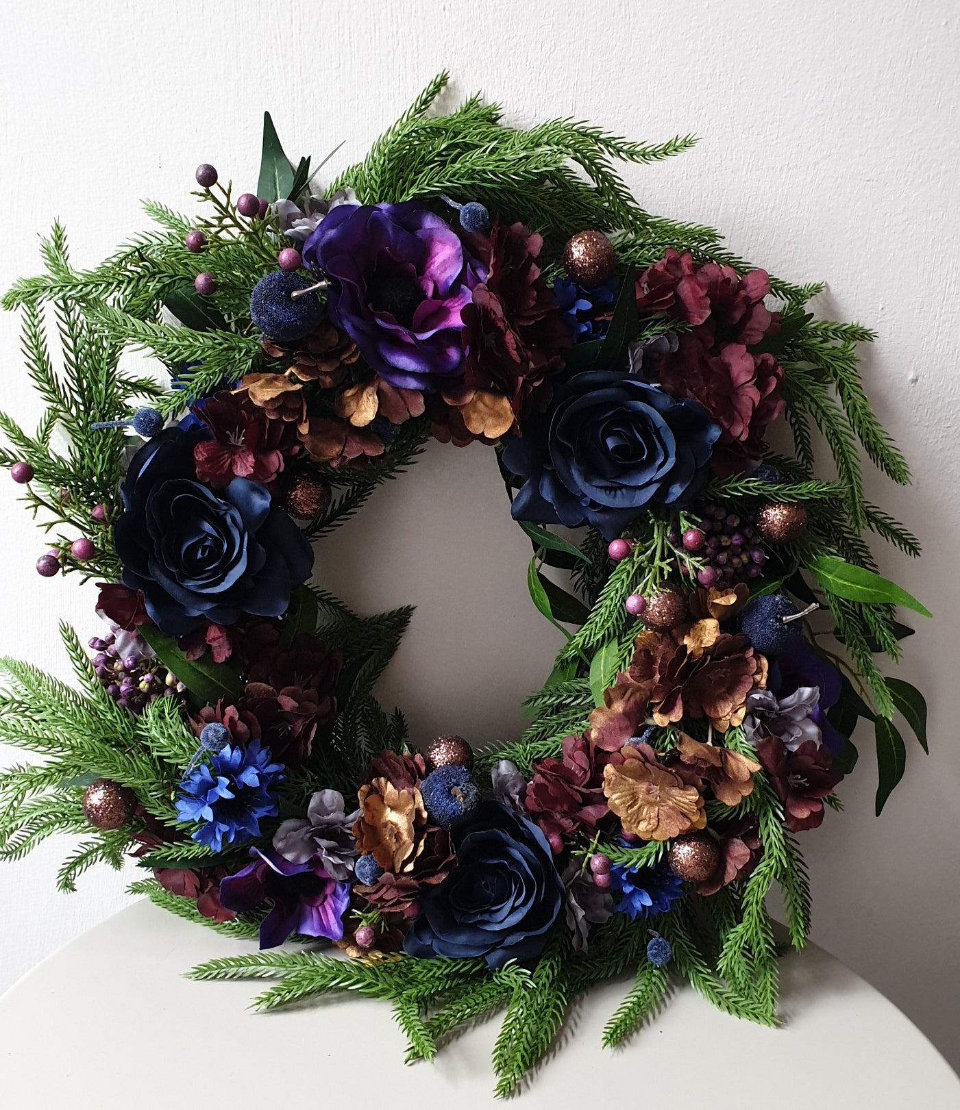 artificial wedding flowers - Decorative wreath with greenery, purple, blue, and gold flowers on a white background