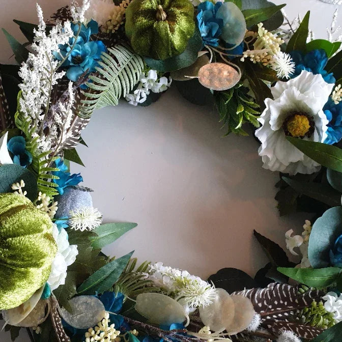 Decorative door wreath Cheshire with blue, green, and white flowers on a plain background