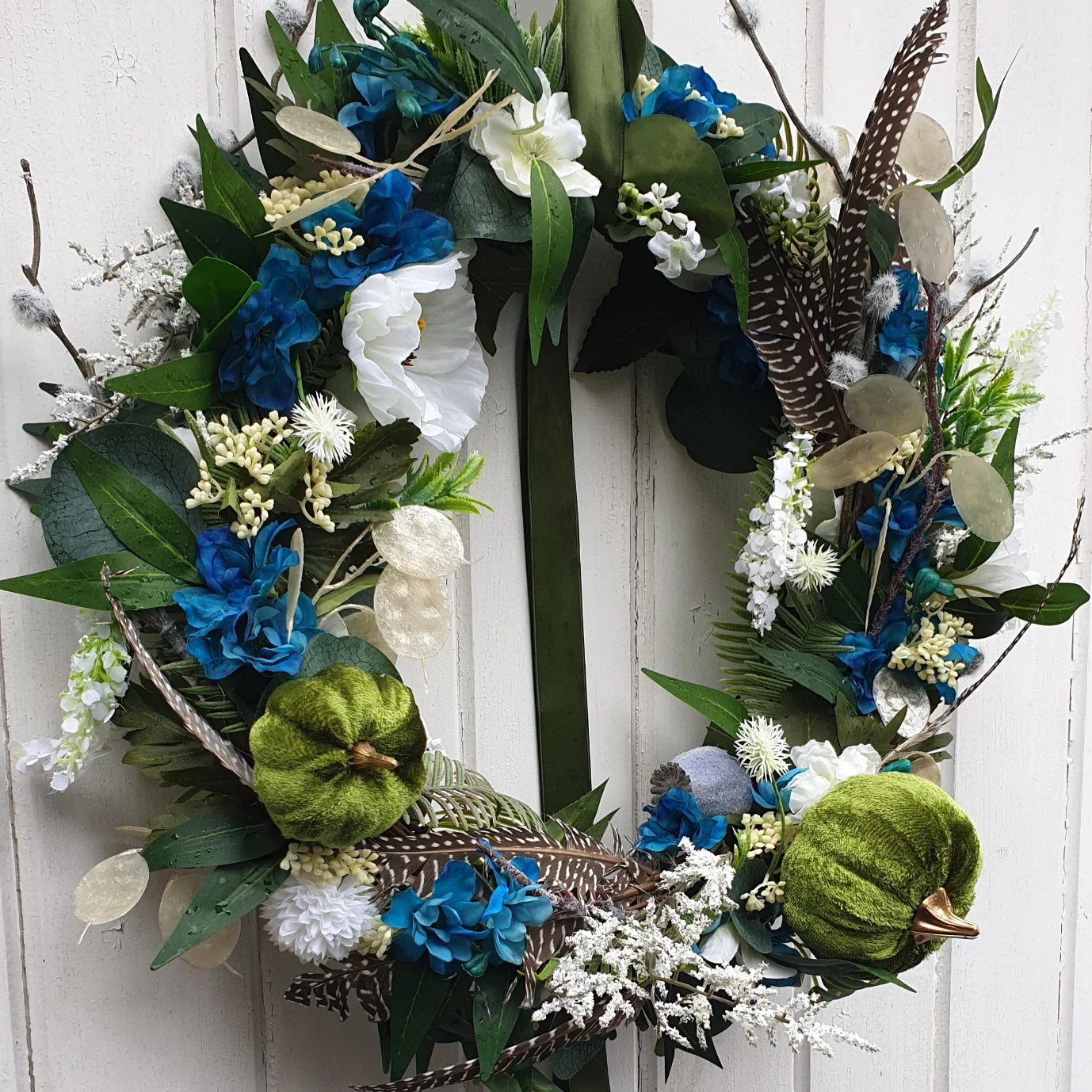 Decorative autumn door wreaths Cheshire with blue, green, and white flowers on a white door.