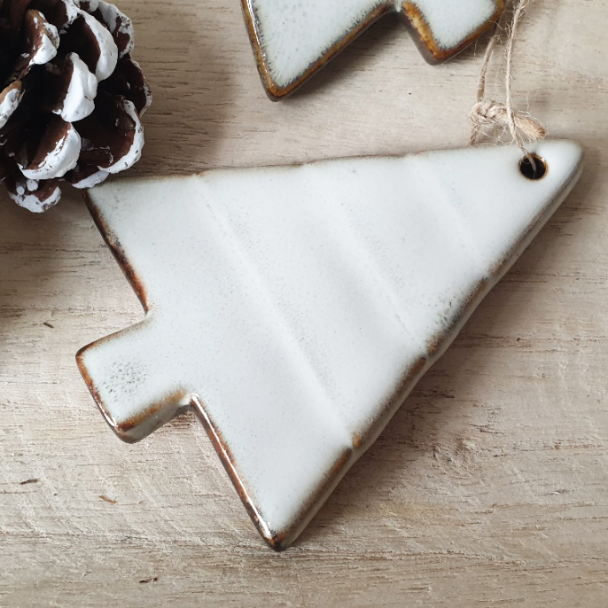 wedding flowers Cheshire - White ceramic Christmas tree ornament on a wooden surface with a pine cone.