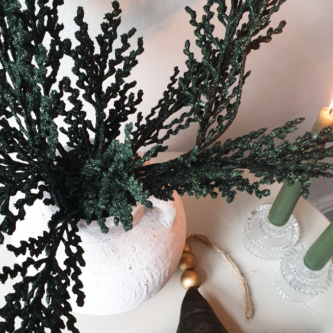 wedding flowers Cheshire - Decorative green branches in a white vase on a table with a candle and gold ornament.