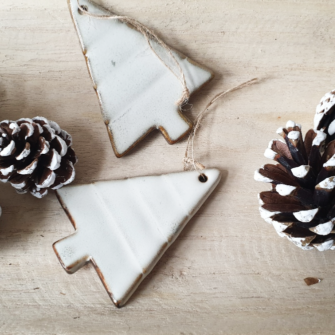 wedding flowers Cheshire - Two ceramic Christmas tree ornaments on a wooden surface with pine cones.
