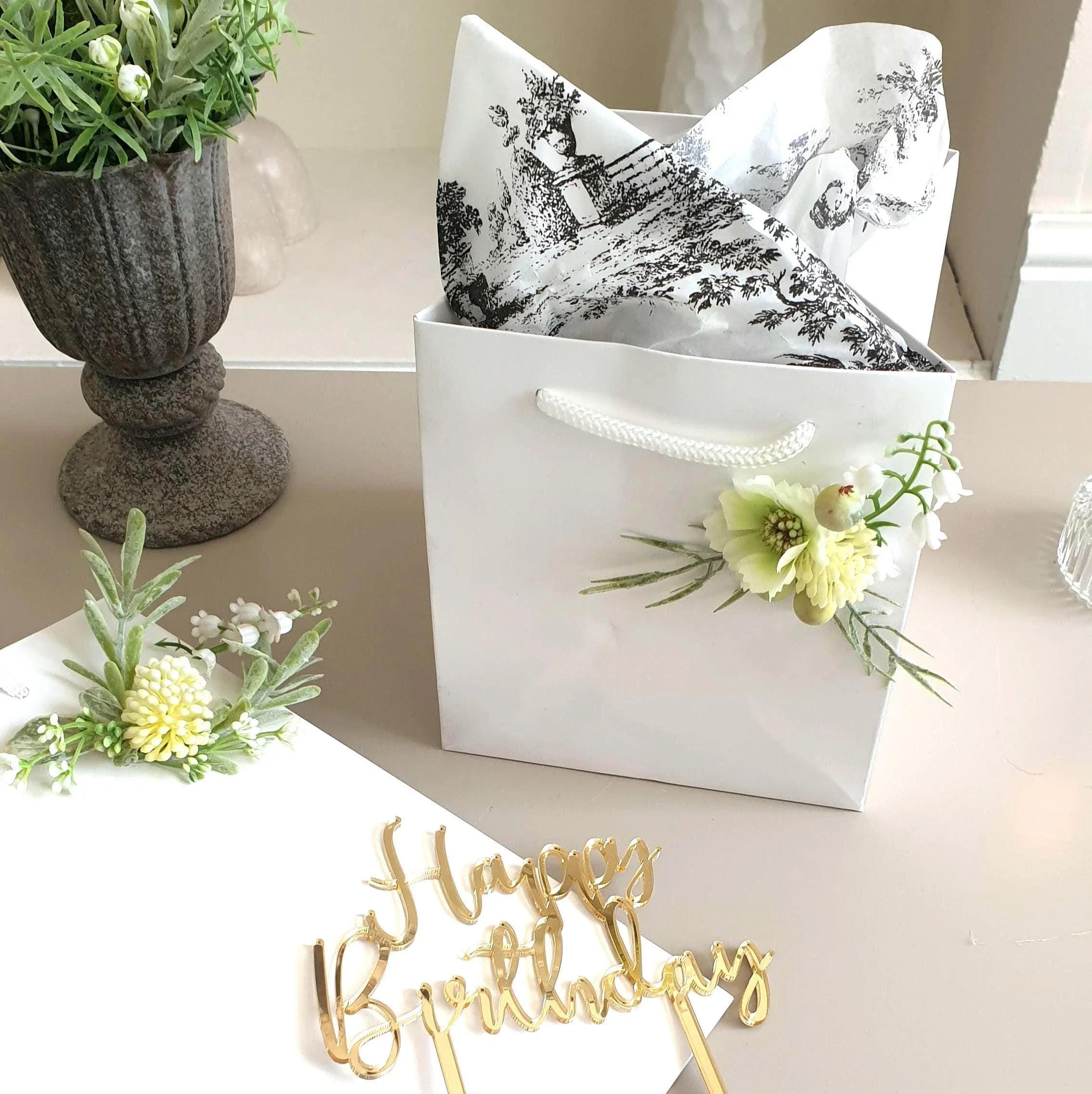 wedding flowers Cheshire - White gift bag with floral design, decorative paper, and   'Happy Birthday' sign on a table.