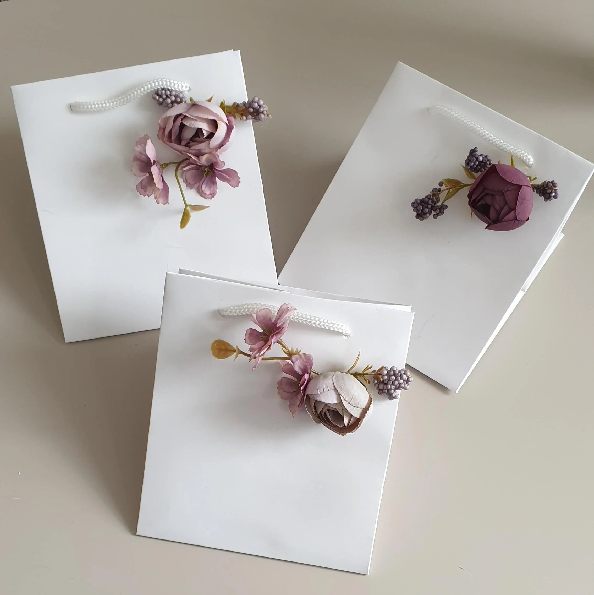 wedding flowers Cheshire - Three white gift bags with floral decorations on a beige background