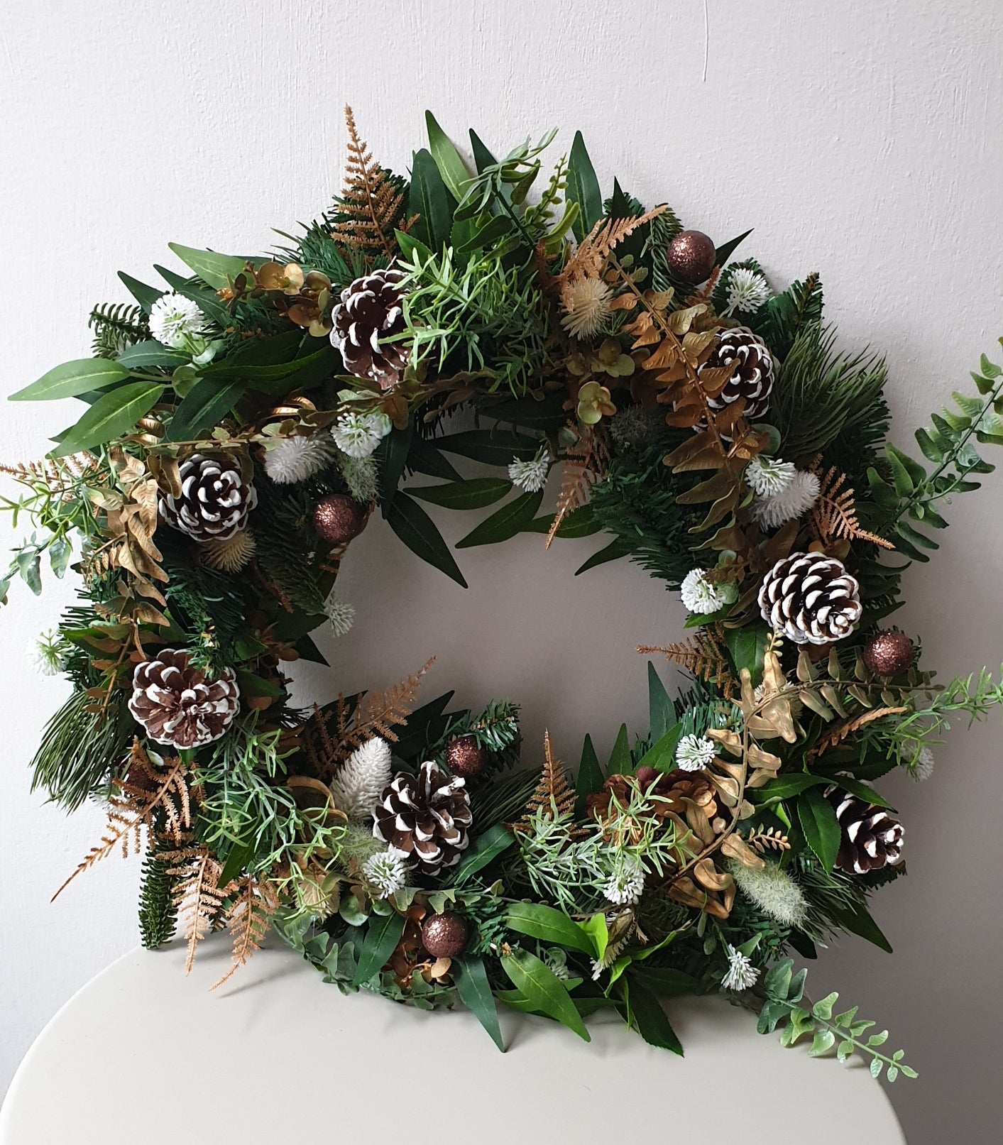 wedding flowers Cheshire - Decorative wreath with greenery, pinecones, and berries on a white surface.