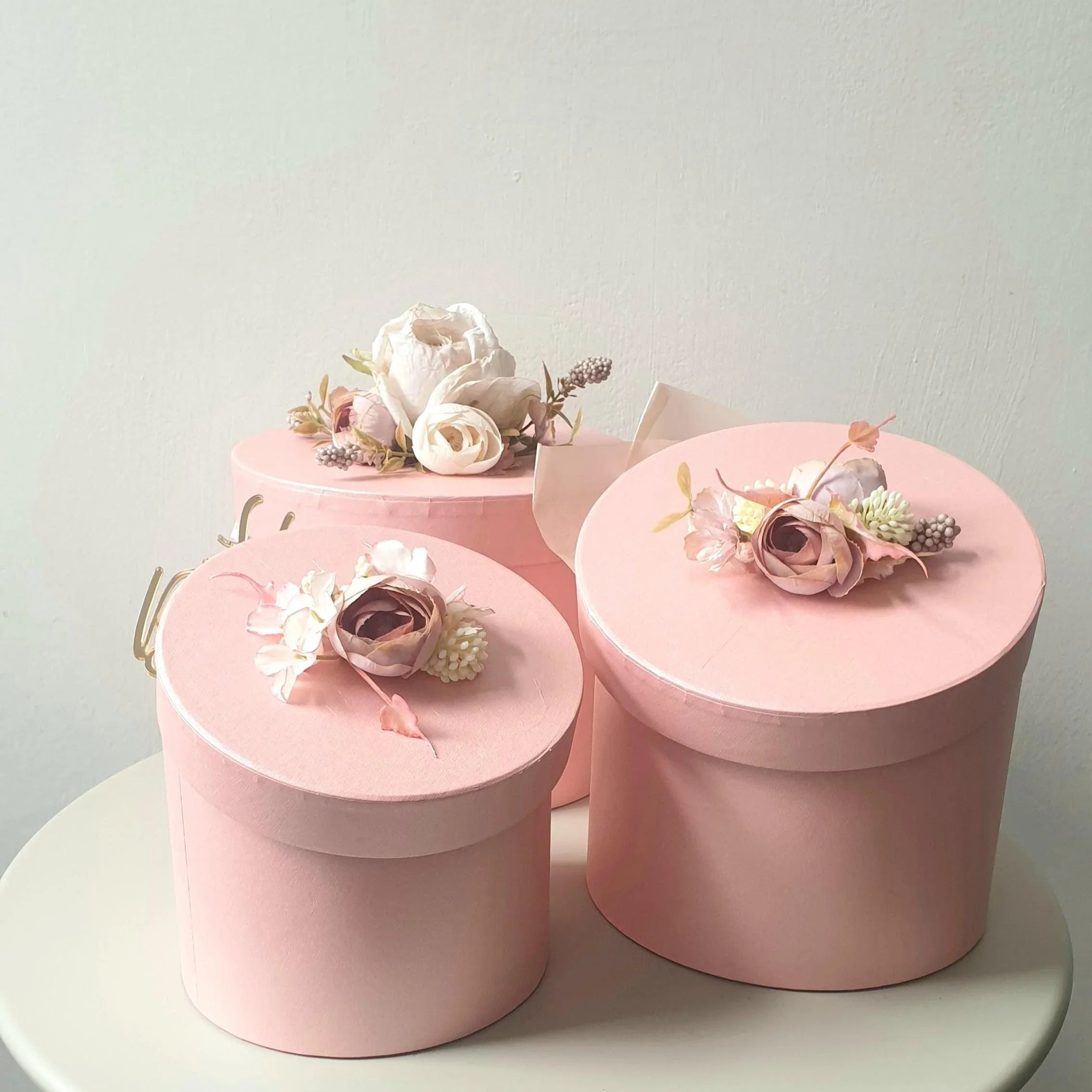 Three pink decorative boxes with floral arrangements on a light gray background