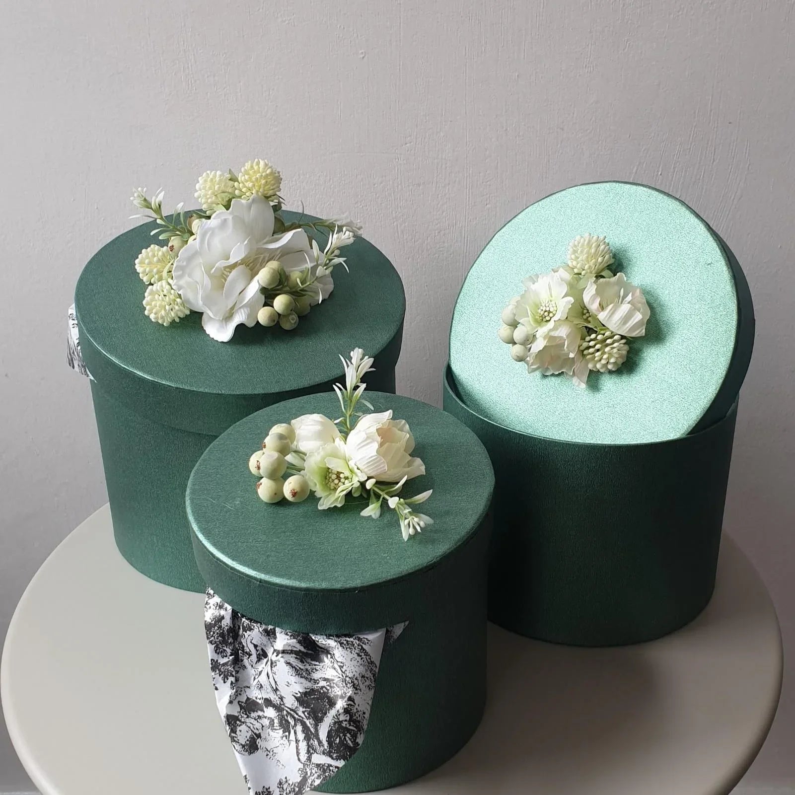 Three green boxes with floral arrangements on a white surface and gray background