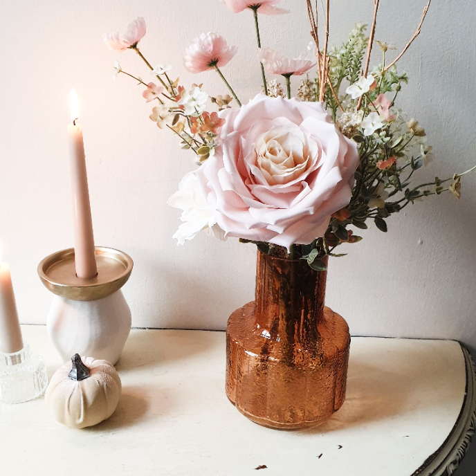 artificial wedding flowers - Copper vase with pink roses and greenery on a white surface with candles and a small pumpkin.