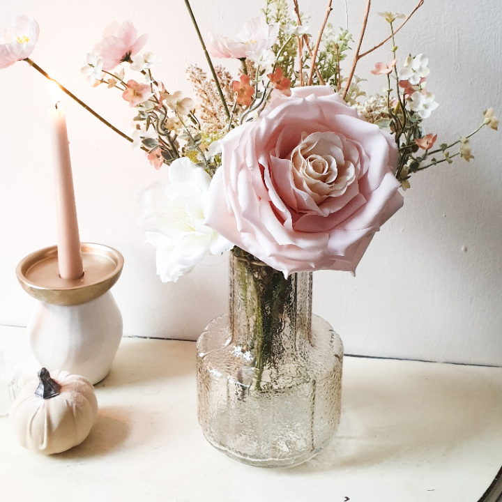 artificial wedding flowers - Glass vase with pink roses and greenery on a white surface
