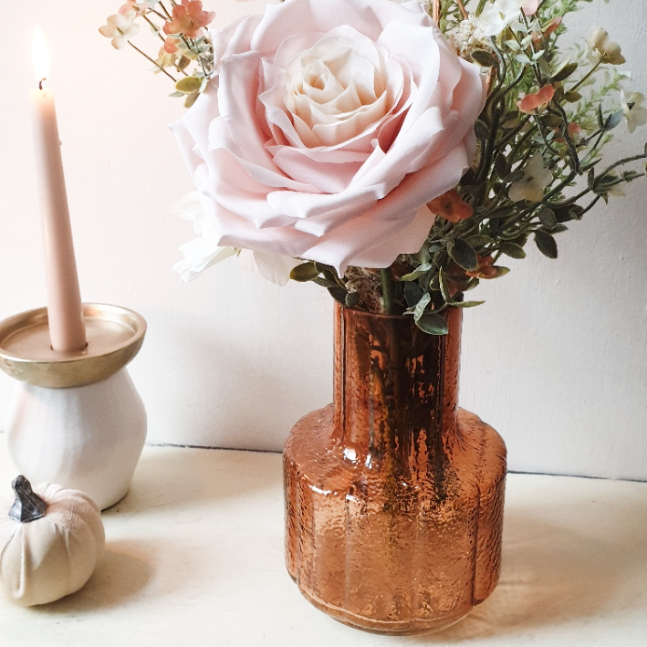 artificial wedding flowers - amber glass vase with pink rose and greenery on a white surface