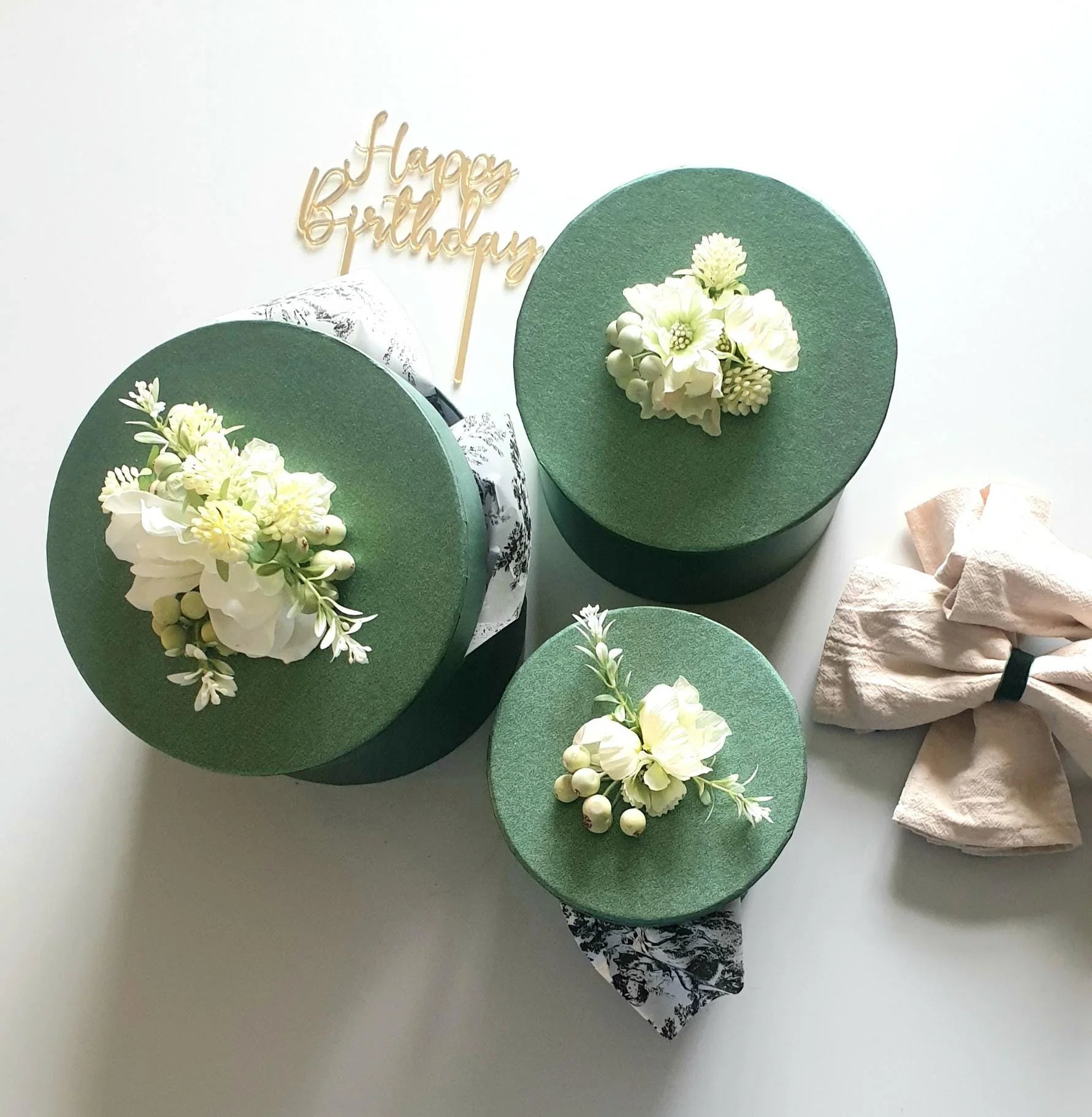 Three green gift boxes with floral decorations on a white background, featuring a 'Happy Birthday' topper.