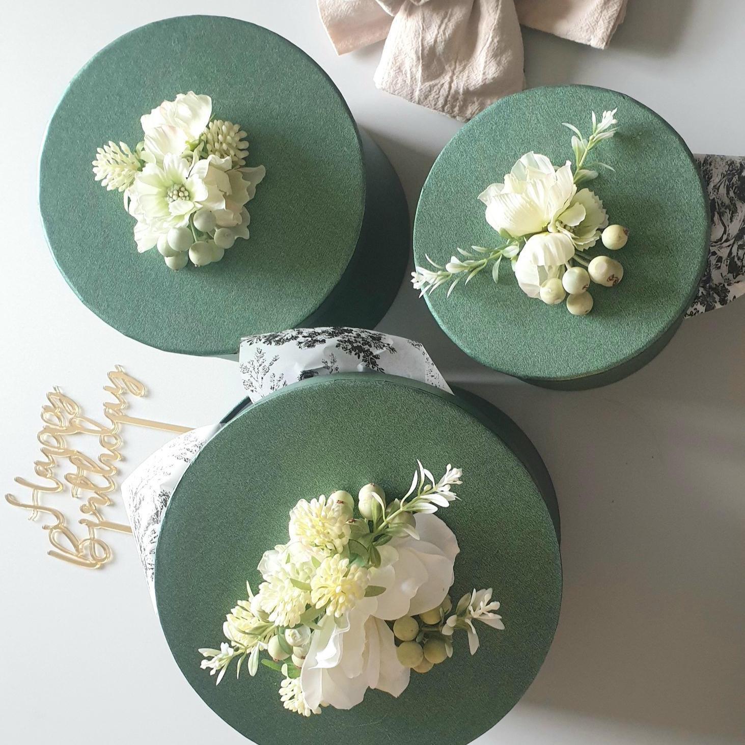 Three green boxes with floral arrangements on a white surface.