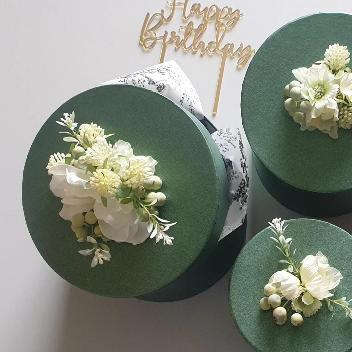 Three green gift boxes with floral arrangements on a white background, featuring a 'Happy Birthday' topper.