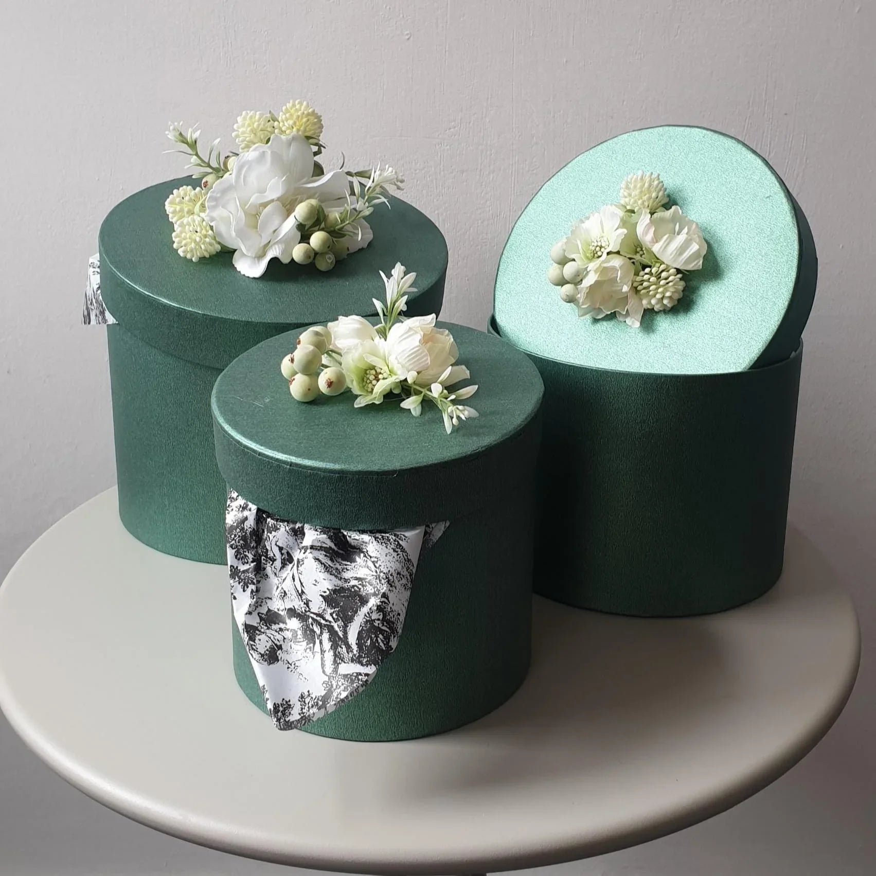 Three green boxes with floral arrangements on a white surface
