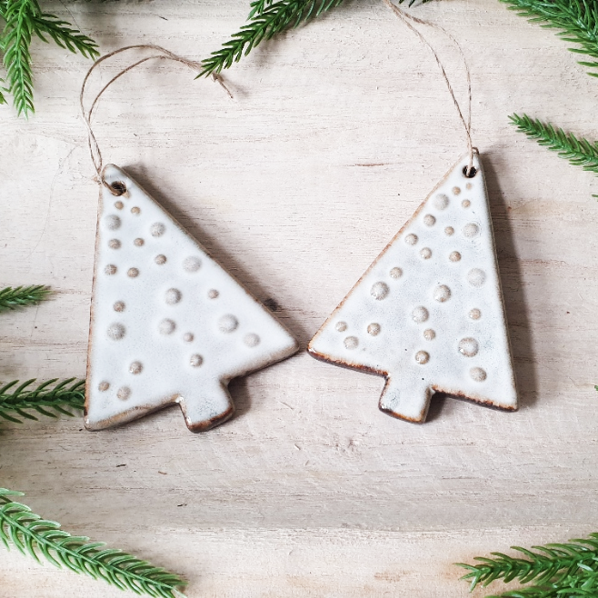 wedding flowers Cheshire - Two ceramic Christmas tree ornaments with a textured surface on a light wooden background with greenery.